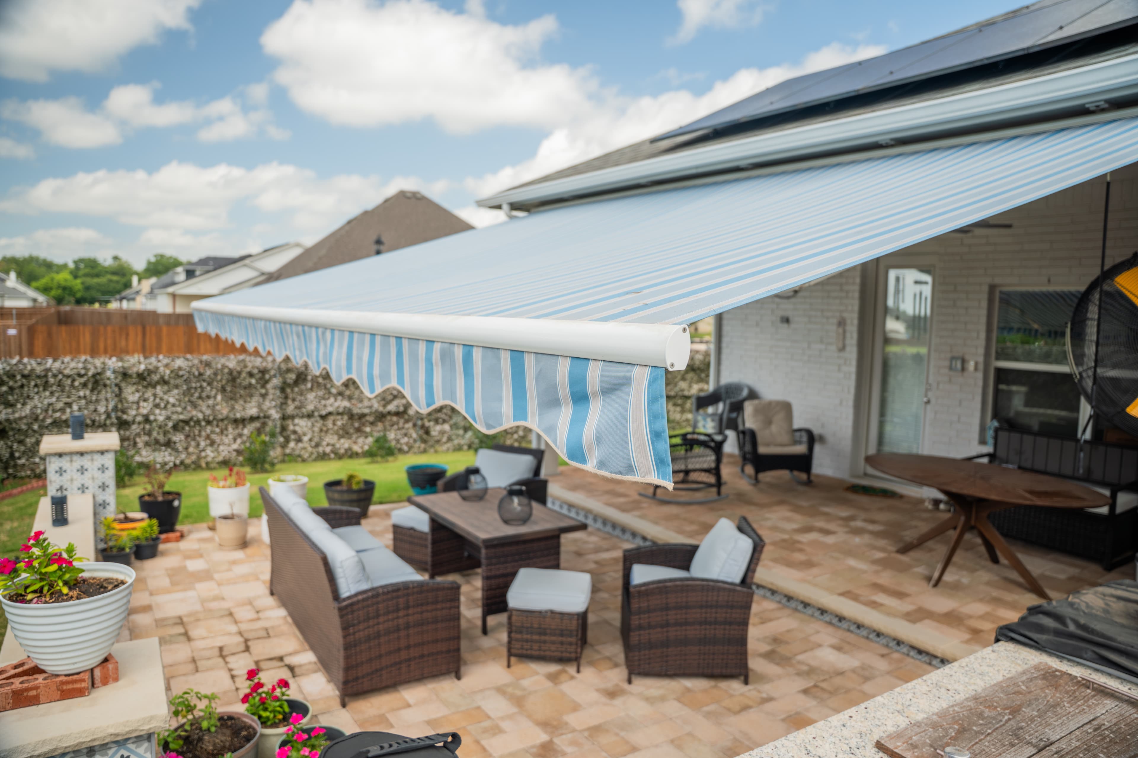 Blue-striped retractable awning fully extended over a paver patio with outdoor seating